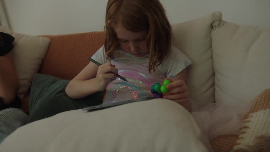 A little girl uses a tablet while sitting on a couch in a living room