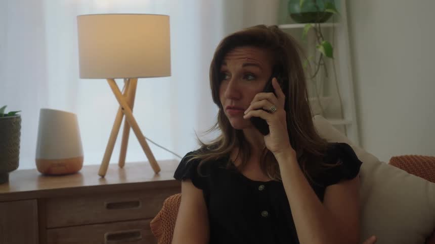 A woman sitting on a couch at home talks on the phone