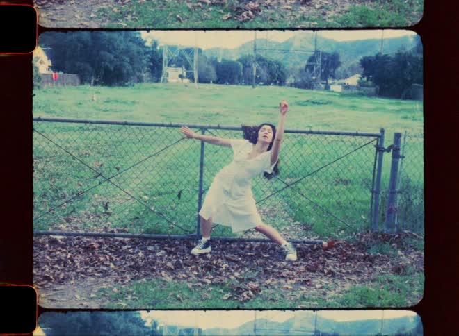 Woman dances while holding onto gate leading to a fenced field in a rural town