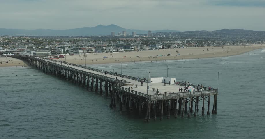 A large pier extends from a beach next to a sprawling city