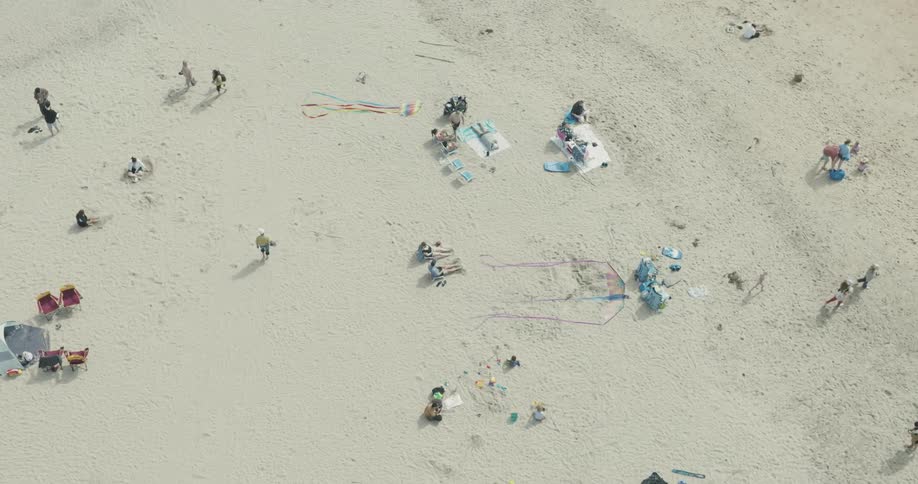 People set up chairs and tents to relax on a beach while others fly kites