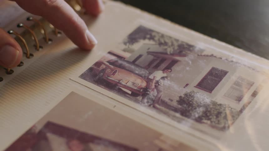 Persons hand runs over old photograph of a man in a photo book