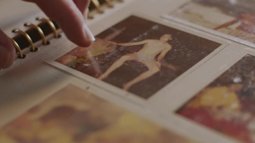 Person runs hand down page of photo album tapping on a couple of old photos
