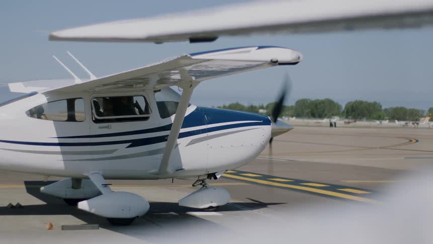 A single engine light aircraft on the ground at an airport with the engine running