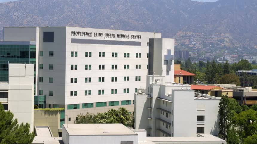 Medical center building is in focus in front of city skyline with mountain range in the background