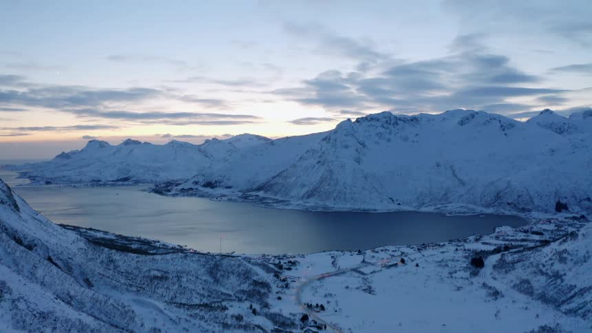 Aerial landscape of snowcovered mountains by a lake against a dawn sky