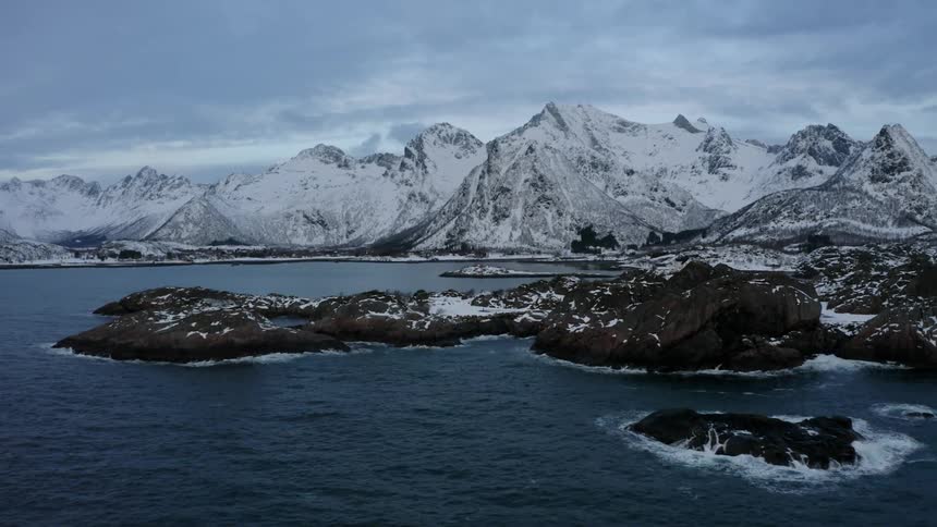 Panorama of mountains covered by snow and surrounded by the sea in a cloudy sky