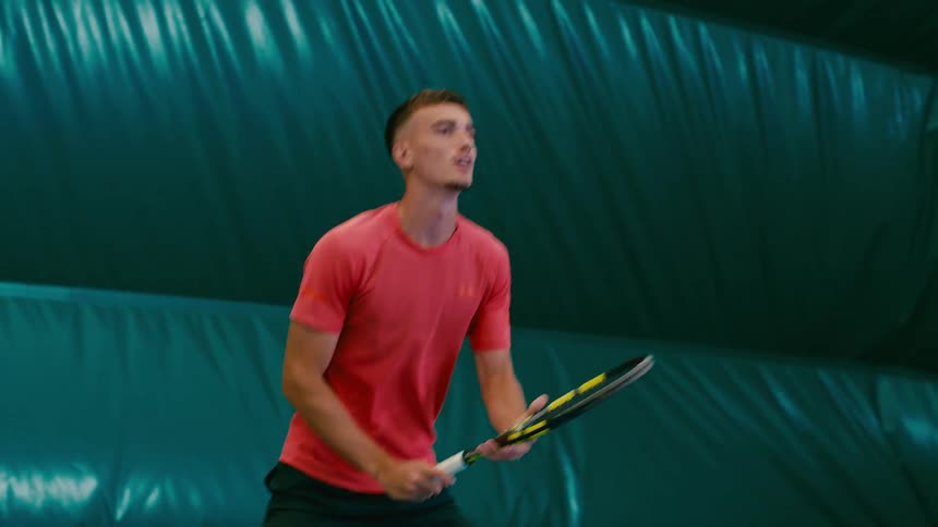 A man is playing tennis while in an indoor building