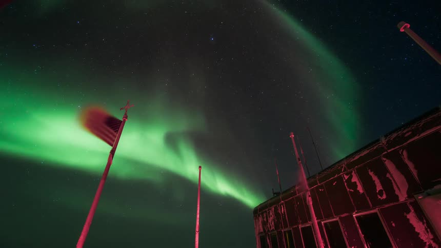 An aurora flashes in the sky over a ruined building a flagpole with an american flag flying from it