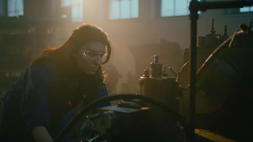 Woman with protective glasses in front of a machine and a metallurgical factory