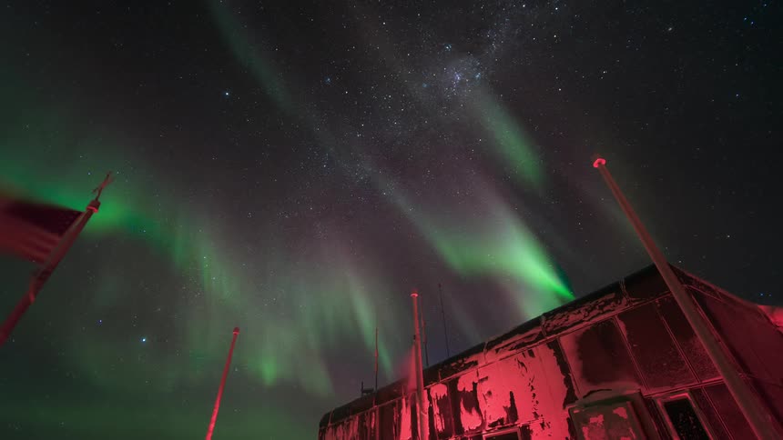 An aurora flashes and twists in a night sky over a wrecked building