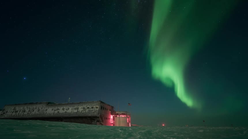 Silhouettes appear and disappear near arctic station while the northern lights move through the sky