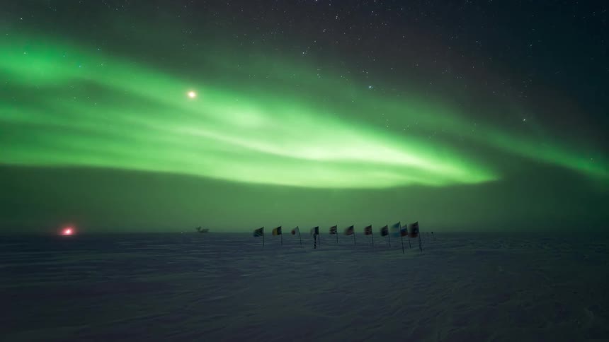 Aurora borealis with shades of green in the night sky over a snowcovered terrain with a line of flags
