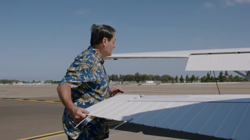 A man inspects the rudder of a small airplane parked on a tarmac