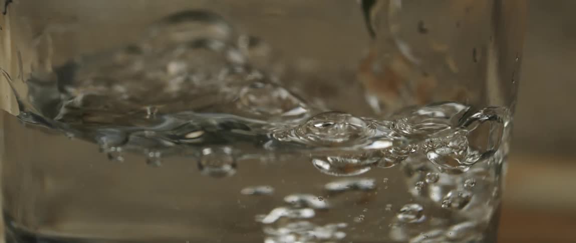 Closeup of a glass cup with water in which water drops are disturbing the liquid surface creating ripples and bubbles