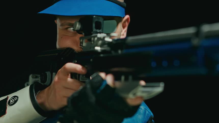 A man is standing outdoors and aiming with a weapon