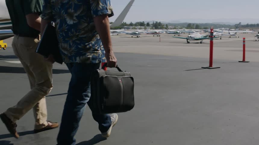 Two travelers walking near airplanes at an airport with small planes