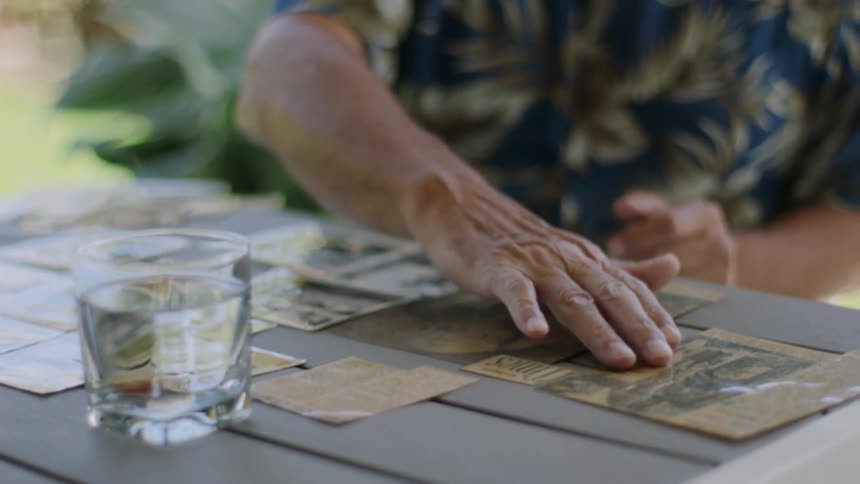 An elderly man lays out an old newspaper article with photo while speaking aloud