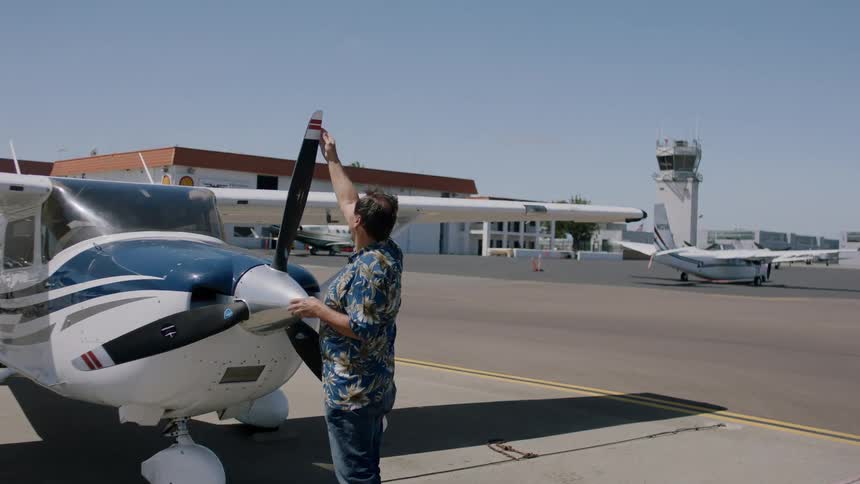 A man stands and wipes the propeller of a small airplane on a tarmac