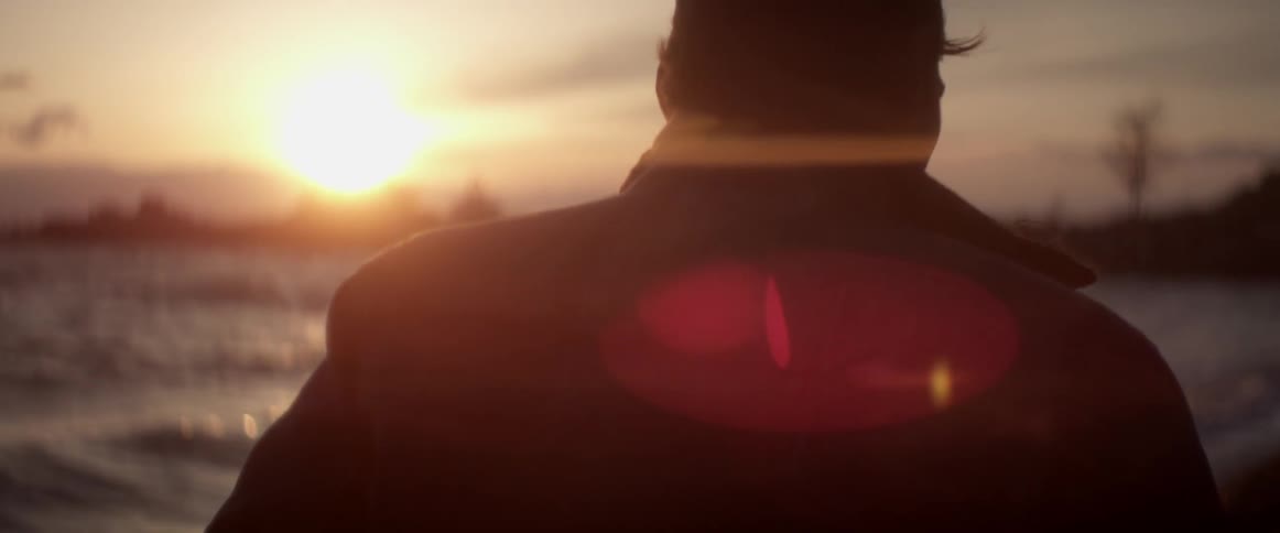 A man wearing a jacket walking on the beach at sunset or sunrise