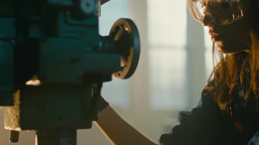 A woman working with a drill press in a dimly lit workshop