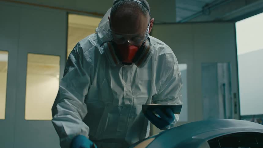 Man with mask and protective glasses using sandpaper and passing over a part of a vehicle
