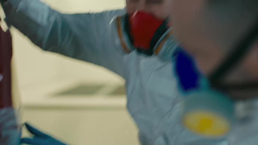 Two men with protective masks talking and analyzing the back of a shaved red car
