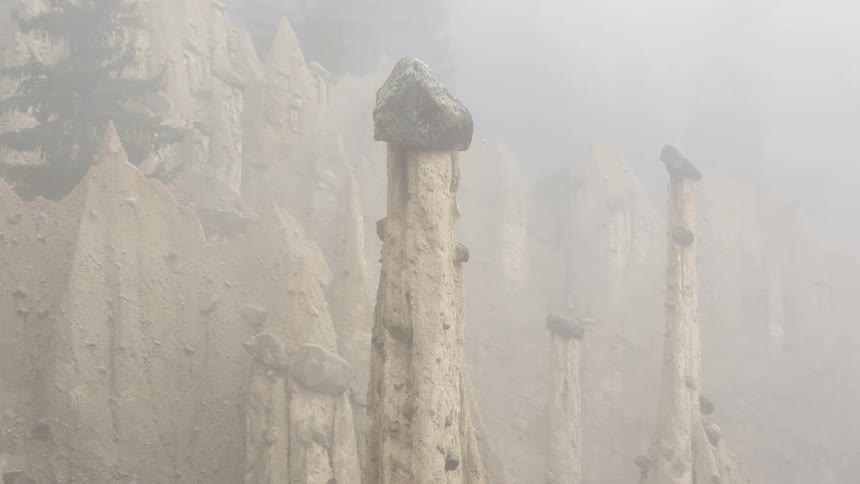 Tall narrow rock formations with pointed tops with a few rocks balanced on top in a hazy environment