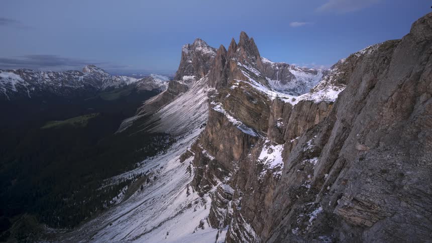 Mountainous landscape with rocky peaks and snowy slopes under a sky that dusk and dawn in time lapse