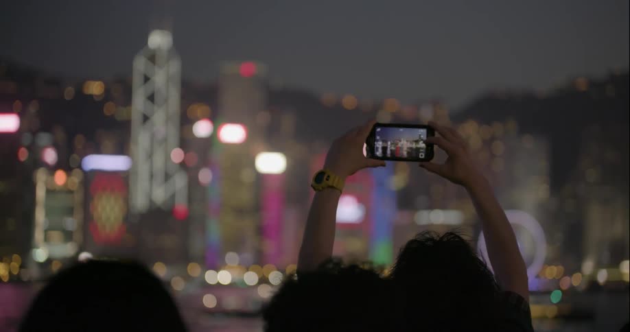A night view of a lit up city and people are filming the buildings on their phones