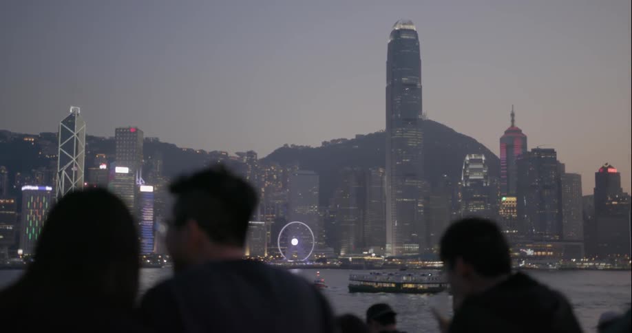 People sit together watching the lit city across the water at sunset