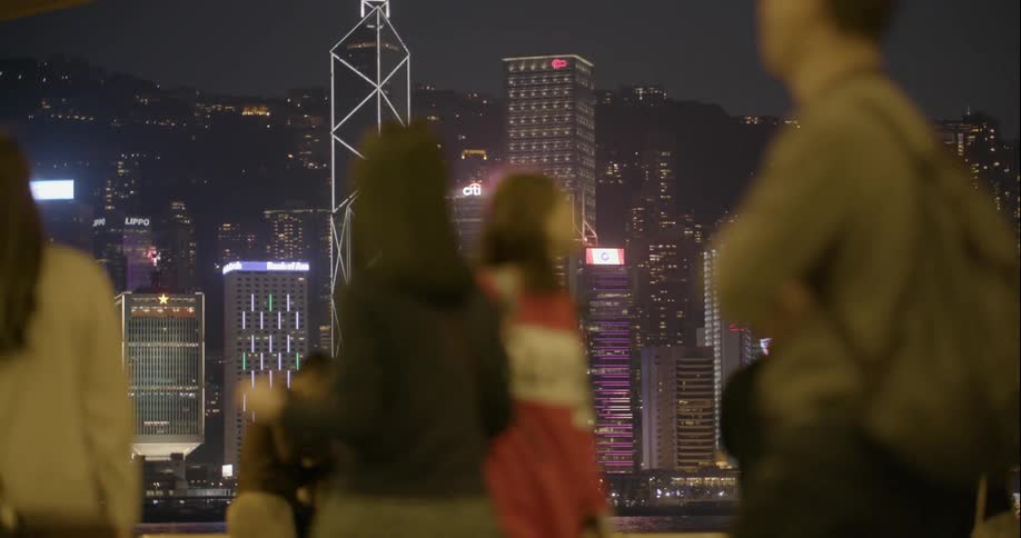 A group of people walk at night around a brightly lit city