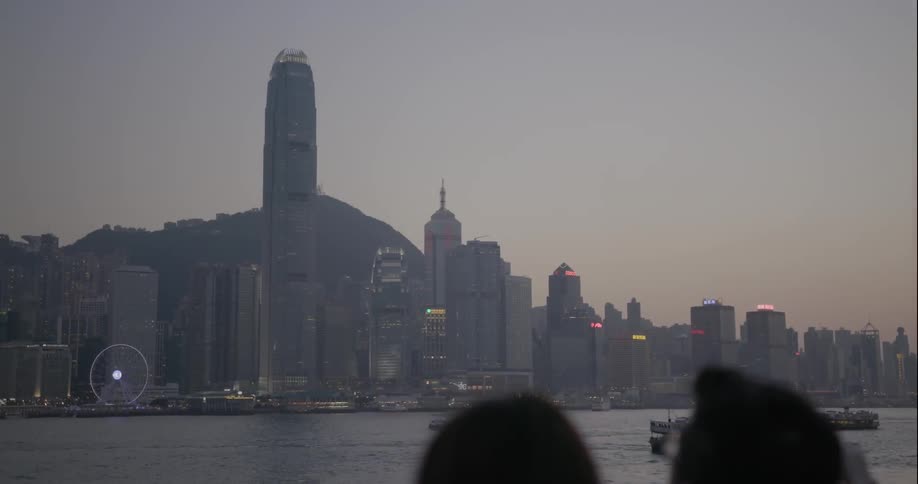 Tourists look at a city from a viewpoint at dusk