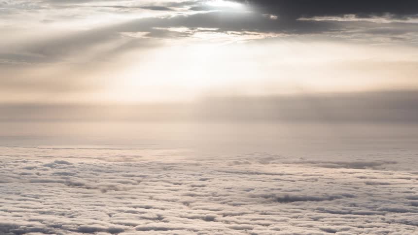 Aerial view of a vast expanse of clouds viewed from above with sunlight filtering through higher clouds