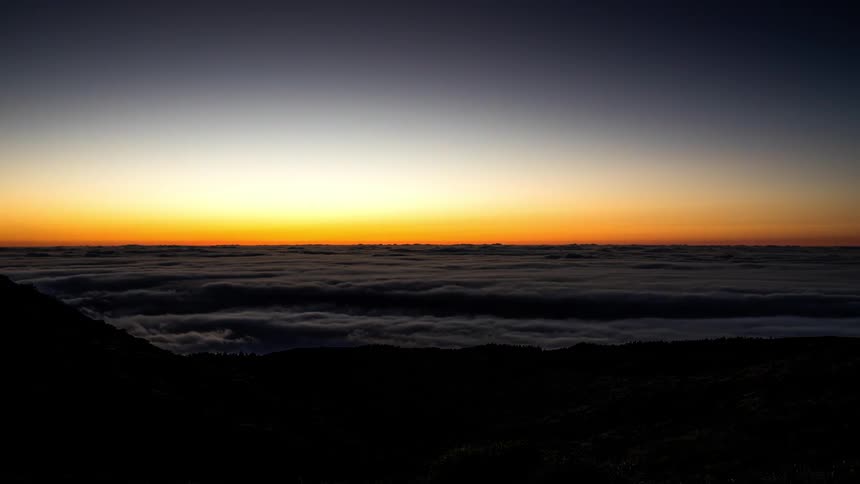 Majestic sunrise seen from the top of a mountain with a sea of clouds below and the day falling into dusk