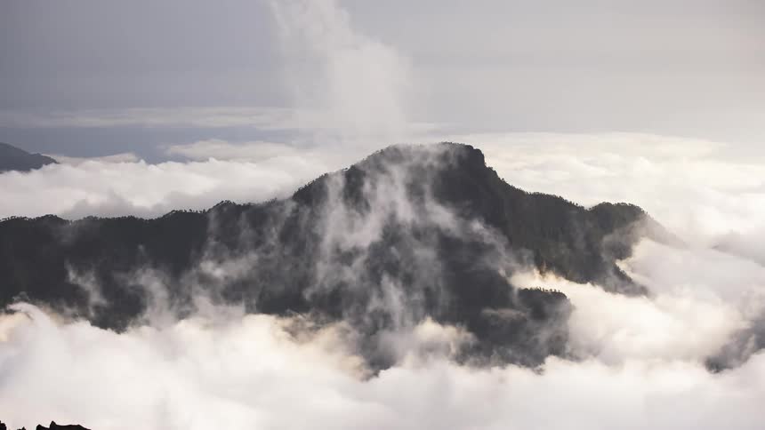 Huge banks of clouds swirl around a forest covered mountain