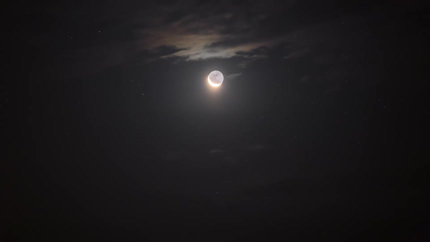 An eclipse takes place in a night sky as clouds roll by