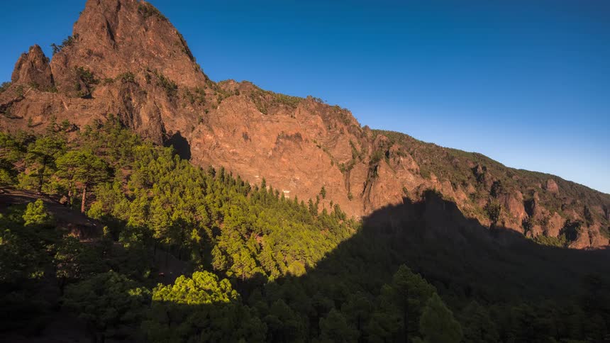 Shadows grow across forest between mountains as day turns into night