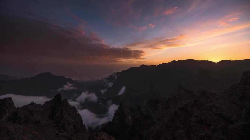 As the sun sinks in the sky dark and white clouds across a mountain range and valley