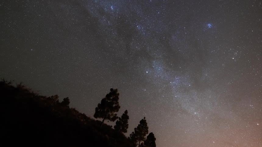 Silhouette of trees on hills and a cloudy sky with stars at night