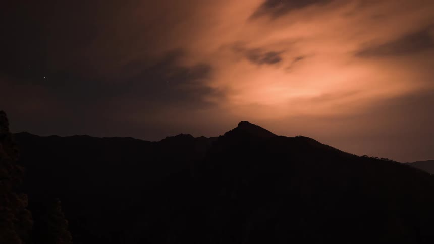 Time lapse of clouds rolling over a mountainous landscape from night to sunrise