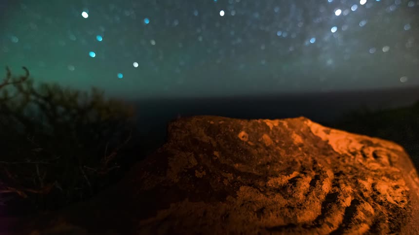 A vast desert landscape under a starry night sky with a prominent carved rock formation