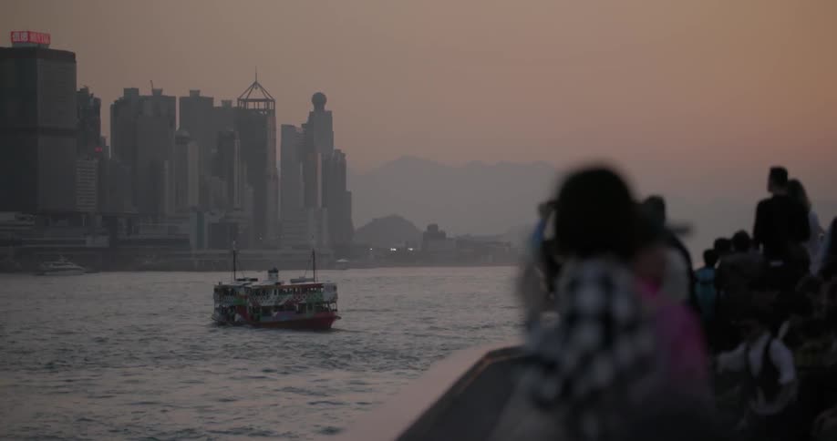 People looking across a river towards a large city as a large boat travels the water