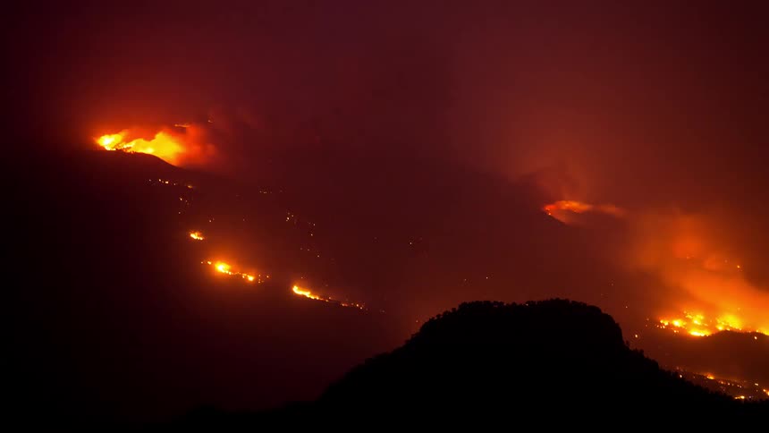 Time lapse of a mountain range with scattered wildfires at night