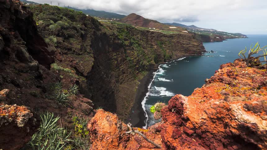 A view of a coast with waves hitting the sand seen from a stone hill