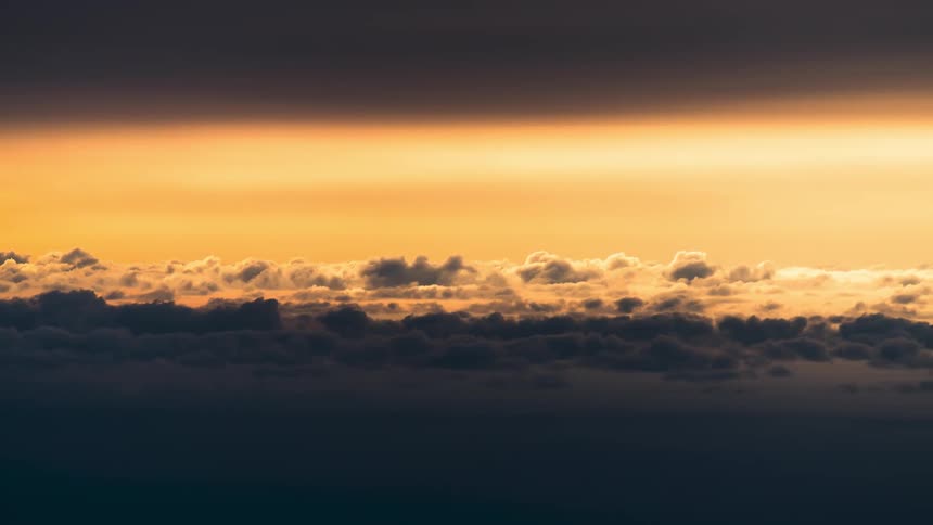 Aerial view of sunlit clouds with a color gradient ranging from orange to dark blue
