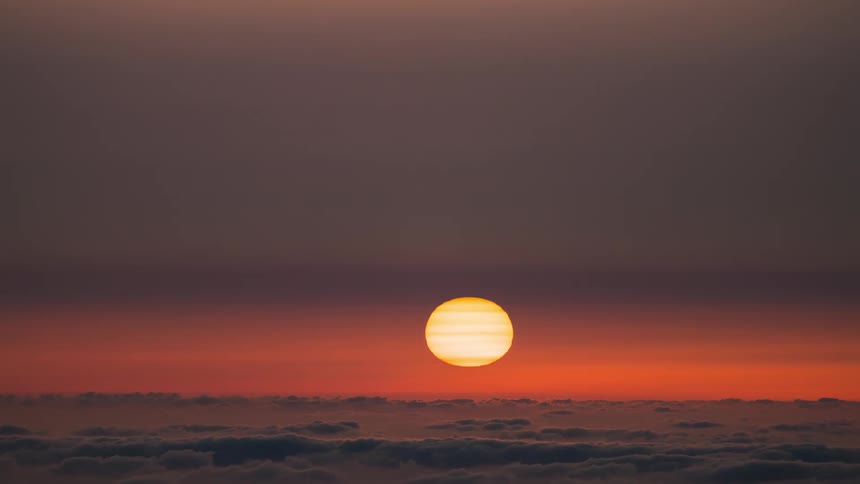 Landscape with the sun setting on the horizon above a sea of dense clouds