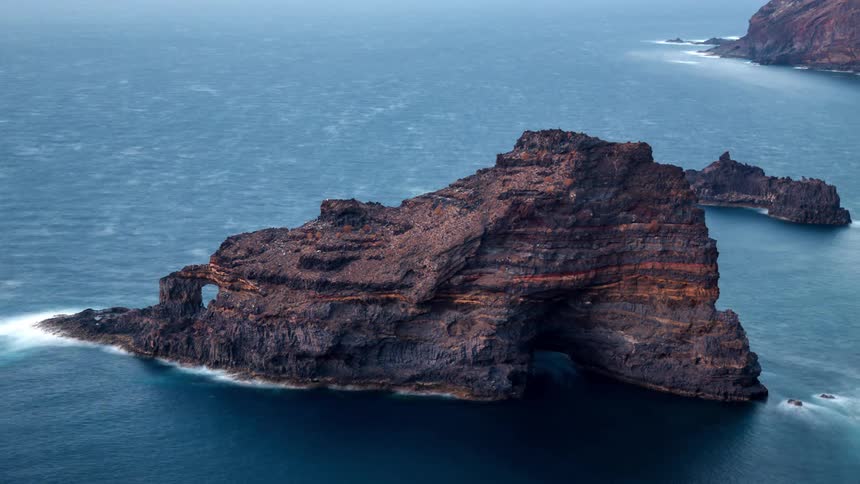 Time lapse of night falling over a rugged rocky island formation in the ocean