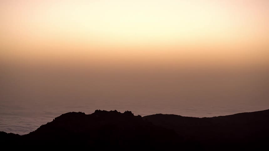 Landscape of a sky with shades of red and a sea of clouds next to silhouettes of mountains