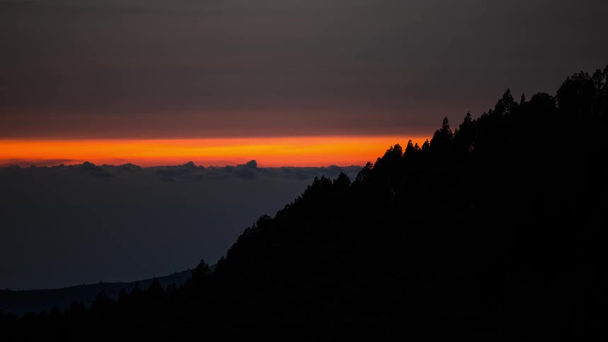 Silhouette of mountains with trees and the reddish sky on the horizon with a sea of clouds